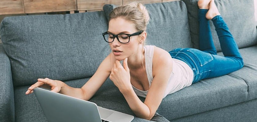 Giovane donna bionda che utilizza il computer portatile sul divano in soggiorno – Come guadagnare con sito porno