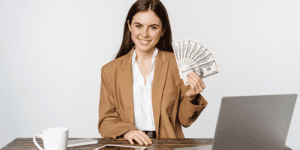 Ritratto di una donna d'affari seduta in ufficio con diverse banconote sulla mano sinistra mentre guarda sorridente la fotocamera