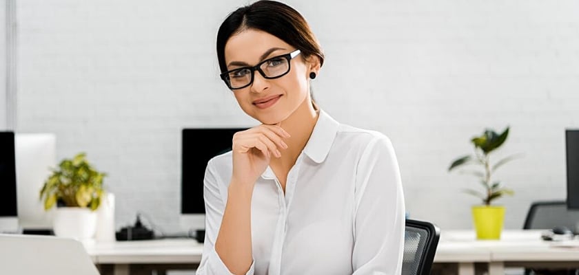 Ritratto di una donna d’affari sorridente con gli occhiali in ufficio che osserva la fotocamera
